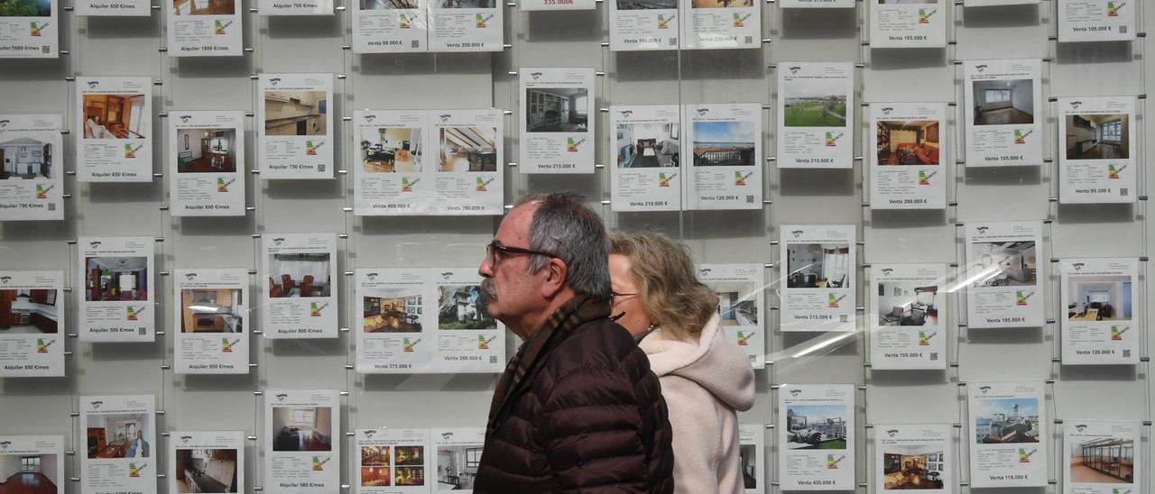 Una pareja pasa frente al escaparate de una agencia inmobiliaria.