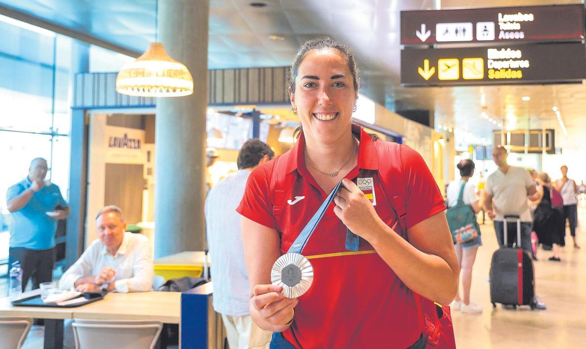 Vega Gimeno, subcampeona olímpica de baloncesto 3x3, posa con su reluciente y pesada medalla de plata a su llegada al aeropuerto de  Manises.