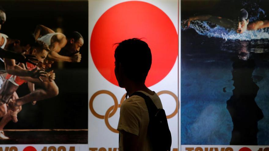 Una persona camina frente a un cartel de los JJOO de Tokio