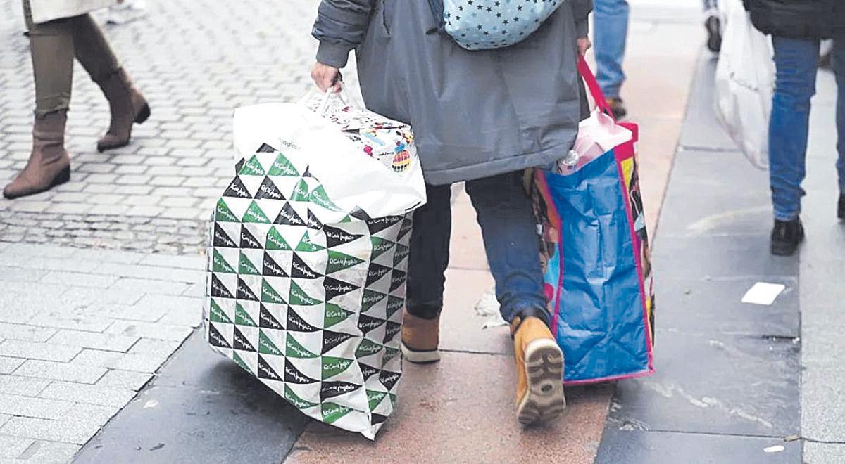 Una persona con bolsas camina por una calle comercial.
