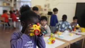 Una niña con una cámara de fotos de juguete en una escuela.
