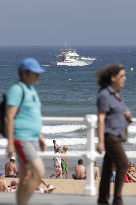 Gijoneses y visitantes se lanzan a la playa en una jornada calurosa.