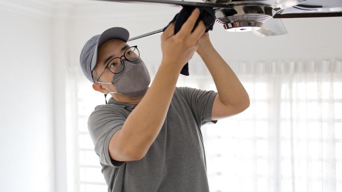 Un hombre limpia un ventilador de techo con un trapo