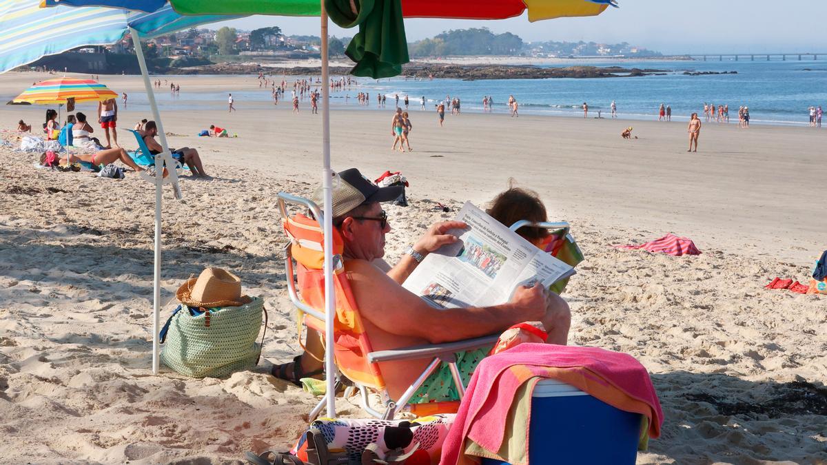 Unha persoa le o Faro de Vigo na praia.