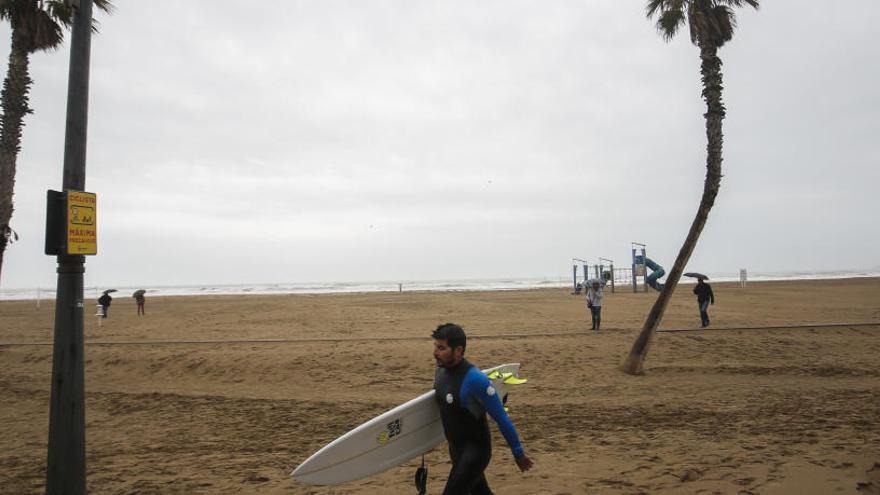 Un surfista en La Patacona, cuyo paseo permanece cubierto de arena.