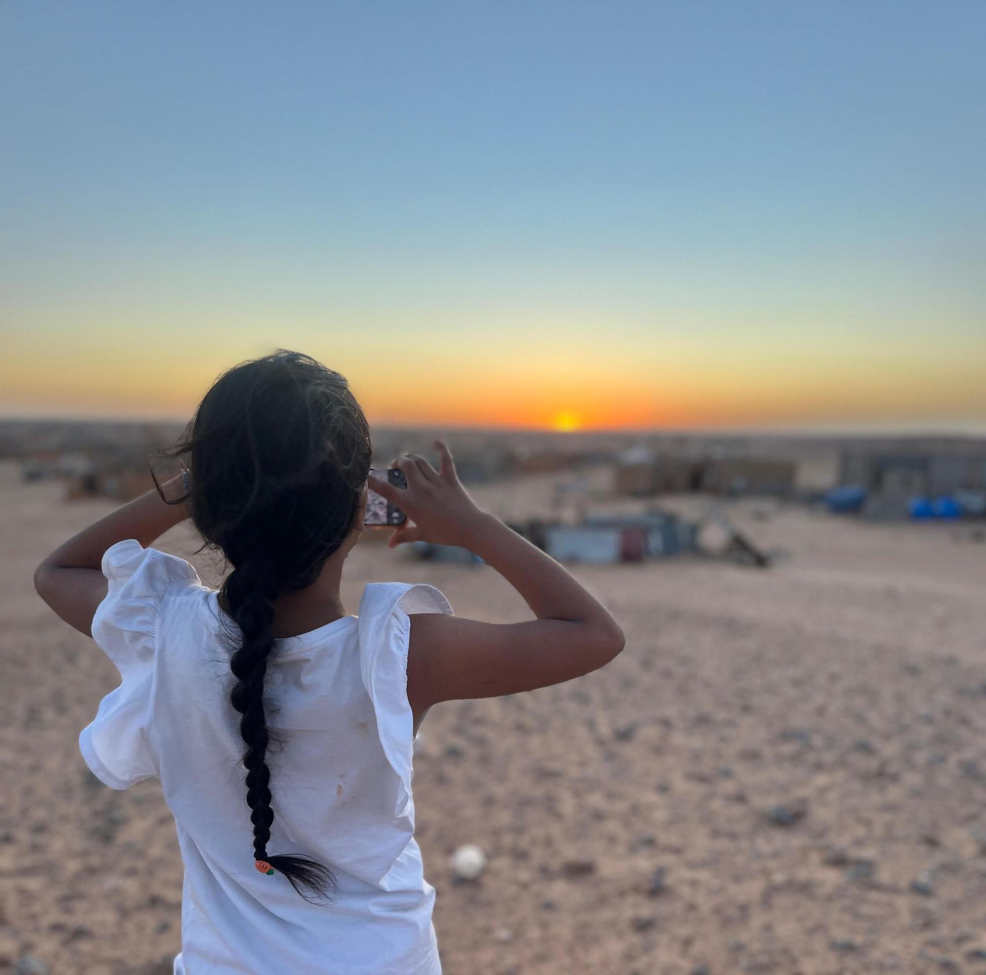 Niña con el campamento de Auserd de fondo en la puesta del sol