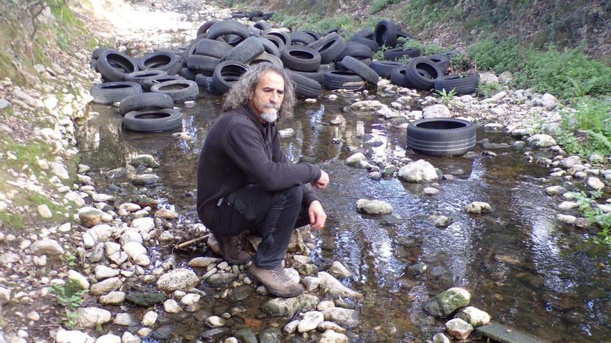 El portavoz de Gadma, Bernat Fiol, junto al vertido de neumáticos en pleno cauce del torrente.