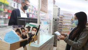 Una joven adquiere un paquete de mascarillas en una farmacia