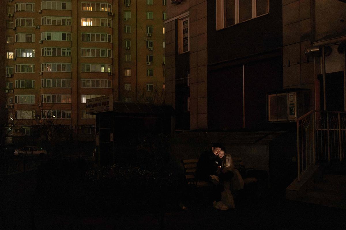 Residentes locales se sientan en un banco con sus teléfonos inteligentes en una calle sin iluminación durante el apagón en Kiev el 10 de diciembre de 2025, tras los ataques con misiles y drones rusos contra la infraestructura energética ucraniana durante la invasión rusa de Ucrania