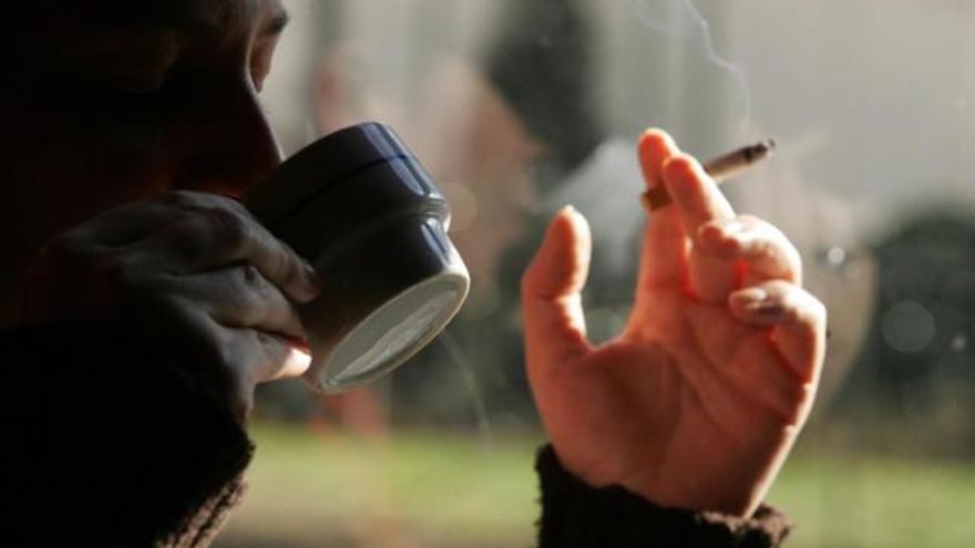 Un hombre se fuma un cigarro mientras bebe un café.