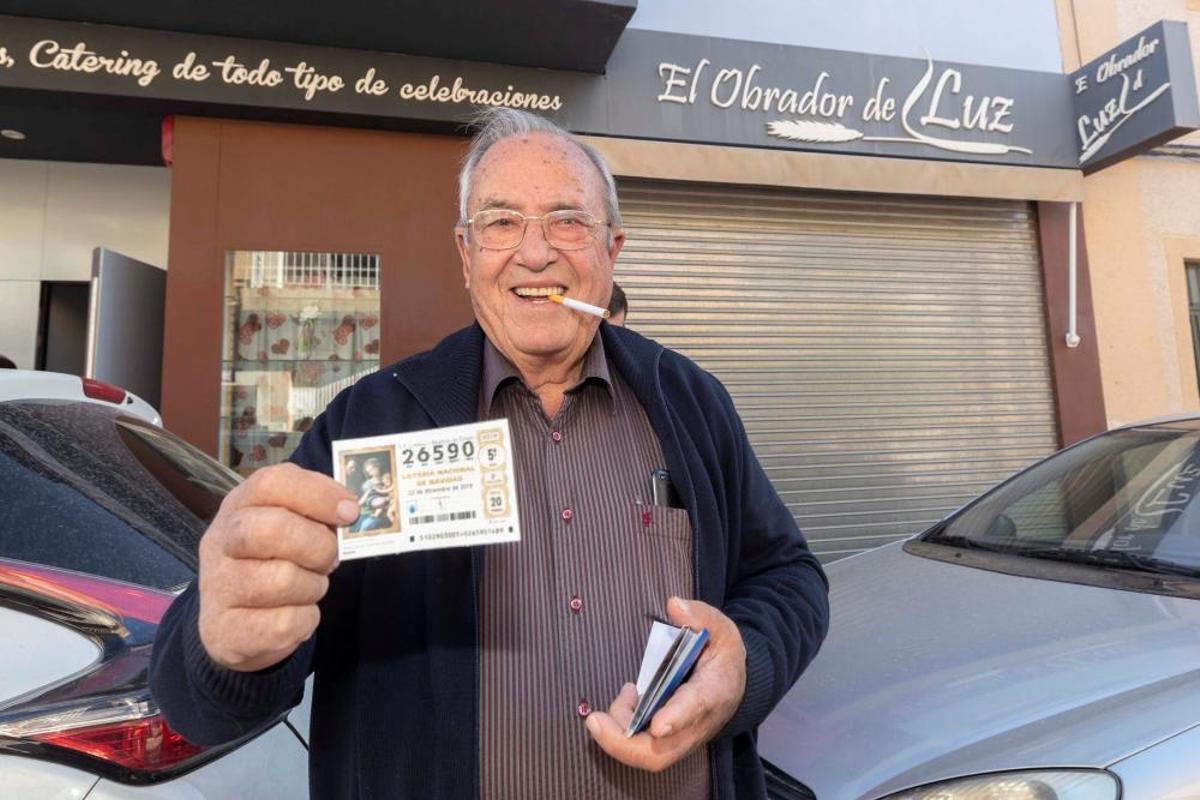 El agraciado con el Gordo de la lotería de navidad Santiago Palazón muestra el décimo premiado junto al obrador donde lo compró en Murcia.