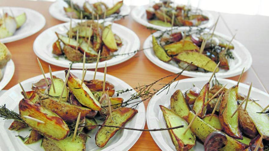 En primer plano, varias tapas de patata al horno con ajos y hierbas del campo como romero y frígola.