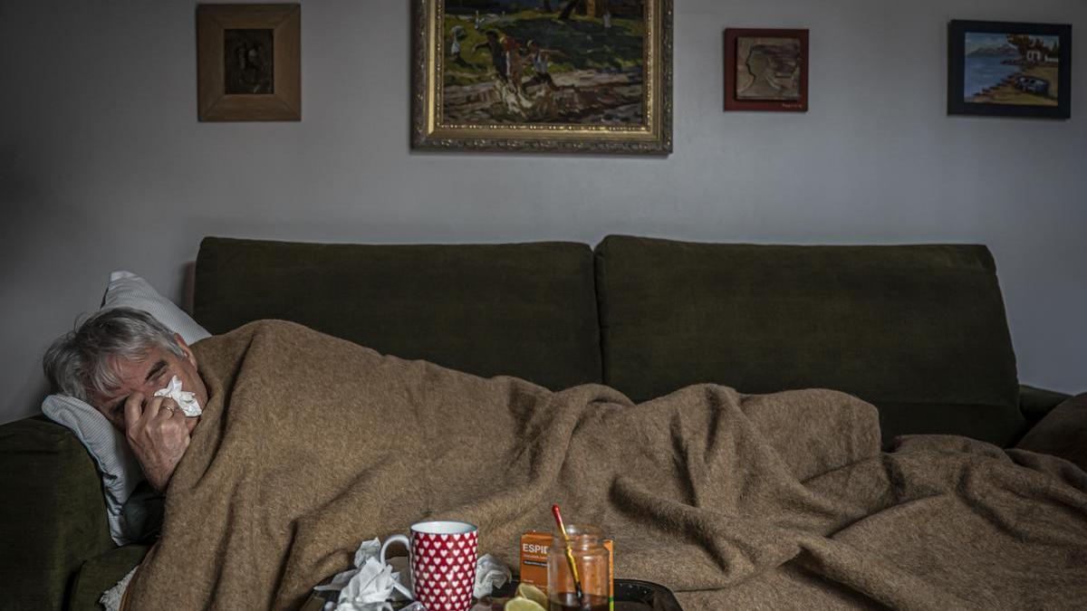 Un hombre con un resfriado en el sofá de su casa.