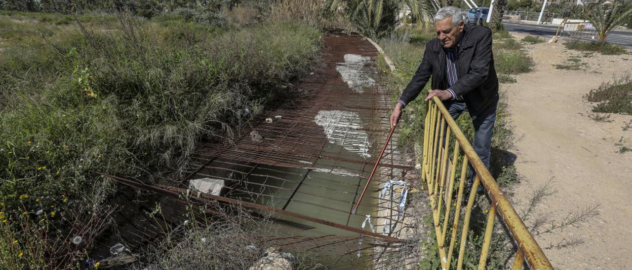 El presidente de la asociación de vecinos, José Gracia, señala con su bastón el hueco entre los hierros que hay en un canal situado junto al puente de la Generalitat.