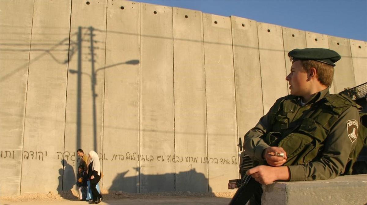 Una familia palestina camina frente a un policía de fronteras israelí, junto al muro que divide en dos la localidad cisjordana de Abu Dis, el 9 de febrero del 2004.