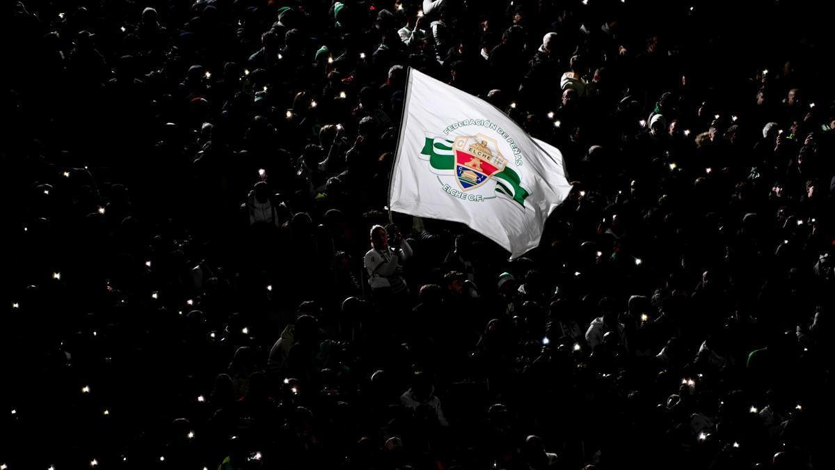 Una bandera con el escudo del Elche es hondeada en las gradas del Martínez Valero, con las luces del estadio apagadas.