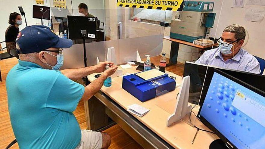 Un ciudadano se limpia ayer con gel, separado con mamparas del funcionario que tramita su DNI.