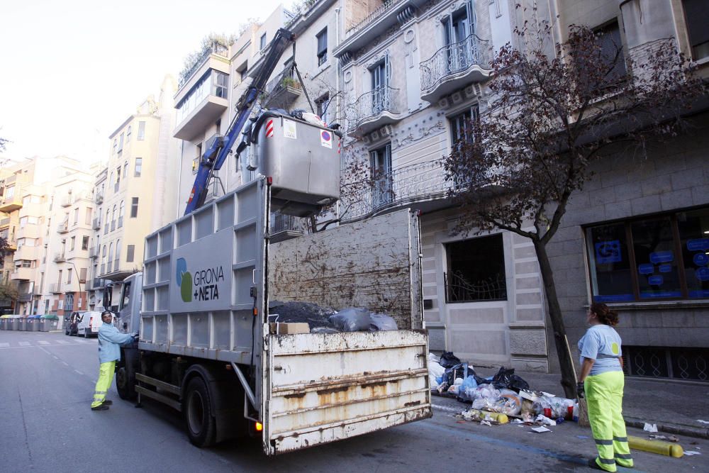 Carrers amb restes de mobiliari urbà cremat, contenidors per terra i treballadors de la brigada treballant