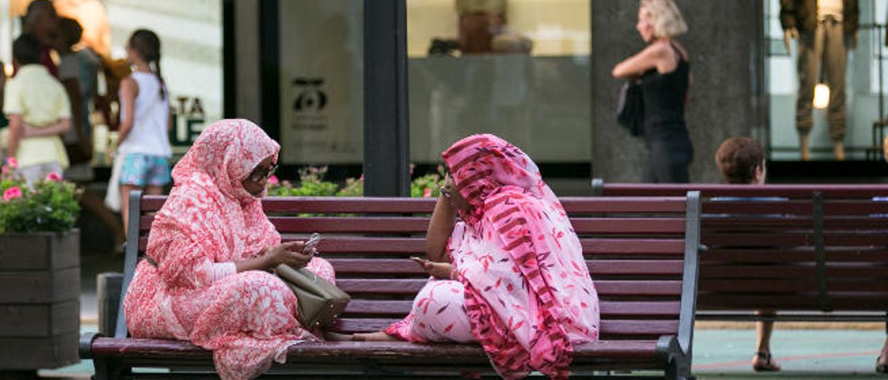 Dos turistas magrebíes se entretienen con su móviles en un banco de la Avenida de Mesa y López.