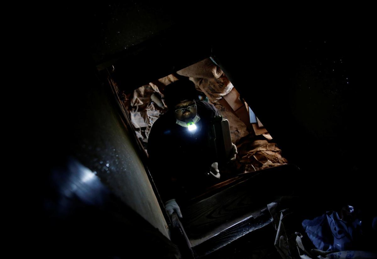 Sakae Kato sostiene una linterna en la boca mientras sube por una escalera al segundo piso de una casa abandonada que Kato convirtió en un refugio para gatos.