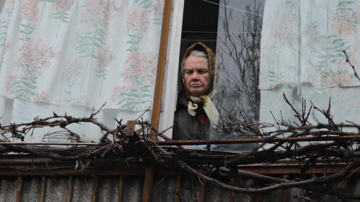 Una mujer se asoma a la ventana de su casa en una calle residencial de Bucha.