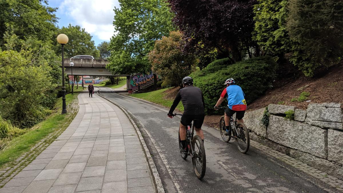 Dos ciclistas circulan por el paseo fluvial del río Bolaños en Arteixo.