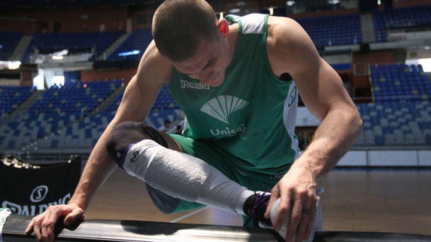 El jugador del Unicaja realiza estiramientos de su rodilla derecha.