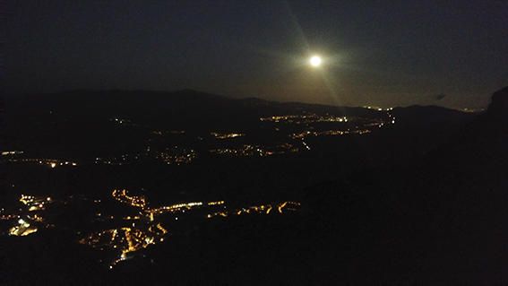 De nit. Resplendor de la lluna plena des de Montserrat i, al fons, tot de llumetes de diferents poblacions.