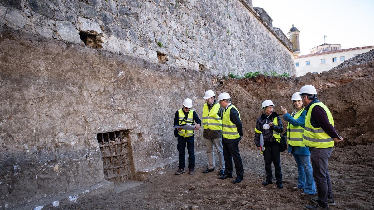 El alcalde junto a los concejales, la arquitecta municipal, el arqueólogo y otro responsable de la obra junto a el tramo de muralla desenterrado donde ha aparecido un desagüe.
