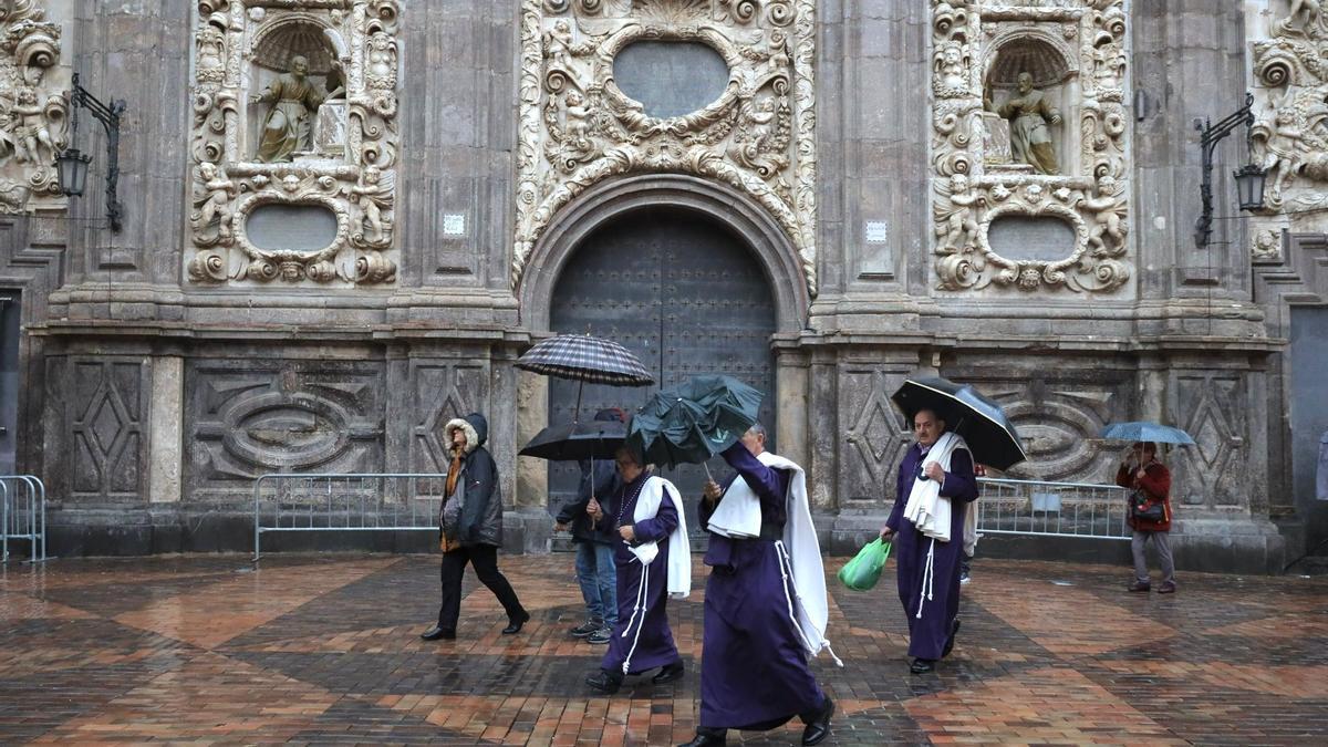 Varios cofrades pasean por la puerta de San Cayetano protegidos por un paraguas