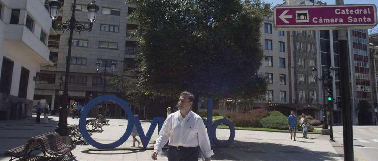 Un hombre deja atrás el letrero de Oviedo, en la plaza del Carbayón, junto a un indicativo de la Catedral.