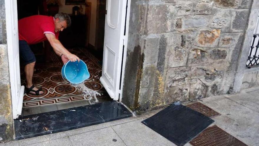 Un vecino achica agua de su vivienda tras una tromba de agua en la calle San Juan el pasado julio.