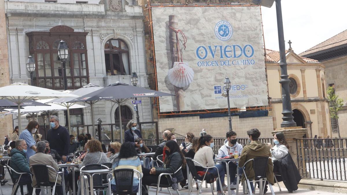 Terraces na plaza de la Catedral, con una lona promocional de “Uviéu, Orixe del Camín” al fondu. | Miki López