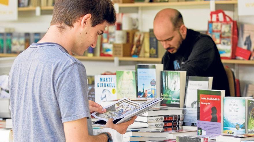 Un joven consulta una obra en una caseta de la Feria del Libro.