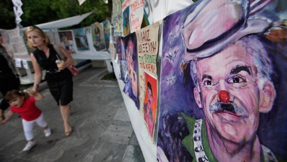 Una dona i una nena passen aquest dimarts a prop d’una caricatura del primer ministre grec, Geòrgios Papandreu, als voltants del Parlament hel·lè, a la plaça Syntagma d’Atenes, on s’estan produint les protestes contra les mesures d’austeritat aprovades a la Cambra.