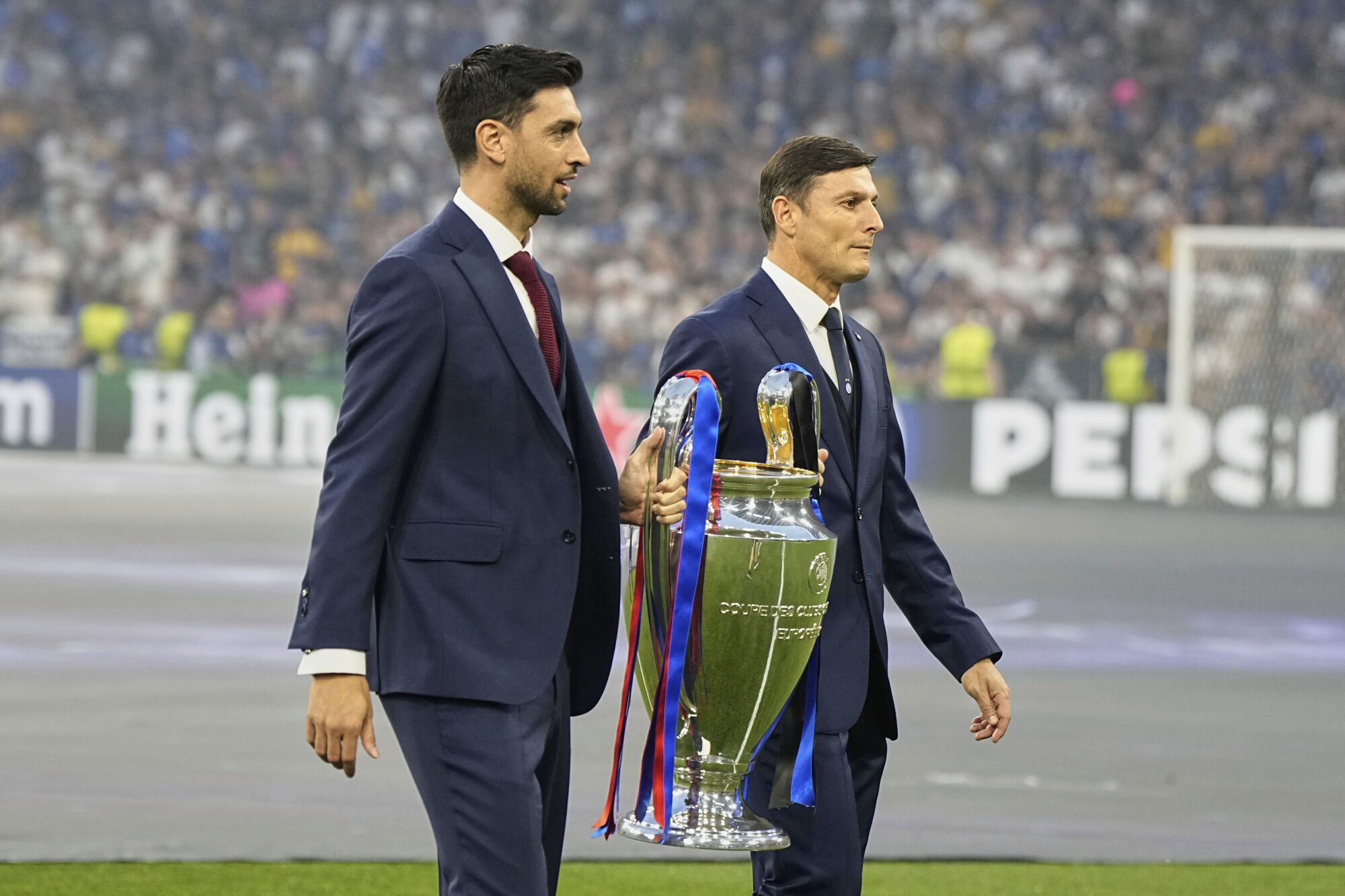 Former PSG player Javier Pastore, left, and Former Inter Milan player Javier Zanetti carry the trophy of the Champions League final soccer match between Paris Saint-Germain and Inter Milan at the Allianz Arena in Munich, Germany, Saturday, May 31, 2025. (AP Photo/Martin Meissner)