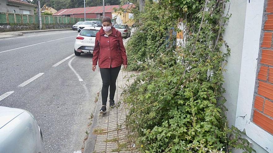 Una persona intenta pasar por la dañada acera llena de zarzas en Mollabao.  | // R. VÁZQUEZ