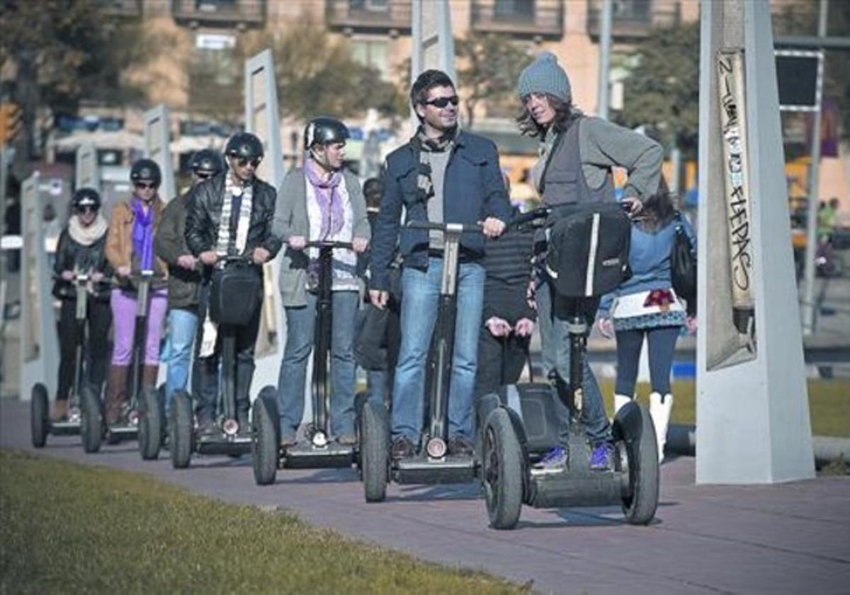 Un grup de turistes condueixen els singulars vehicles de dues rodes al costat del port de Barcelona, ahir.