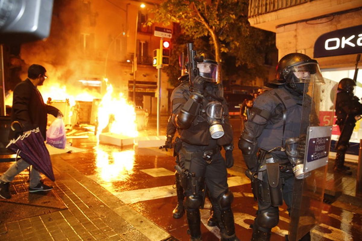 Agents antiavalots bloquegen un carrer mentre al darrere cremen uns contenidors, aquesta nit, a Sants.