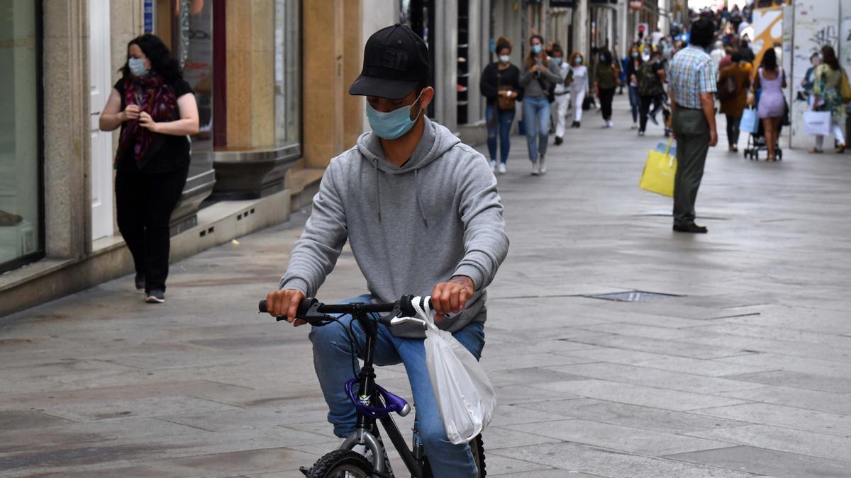 Un hombre con mascarilla, en bicicleta, por la calle Real de A Coruña.