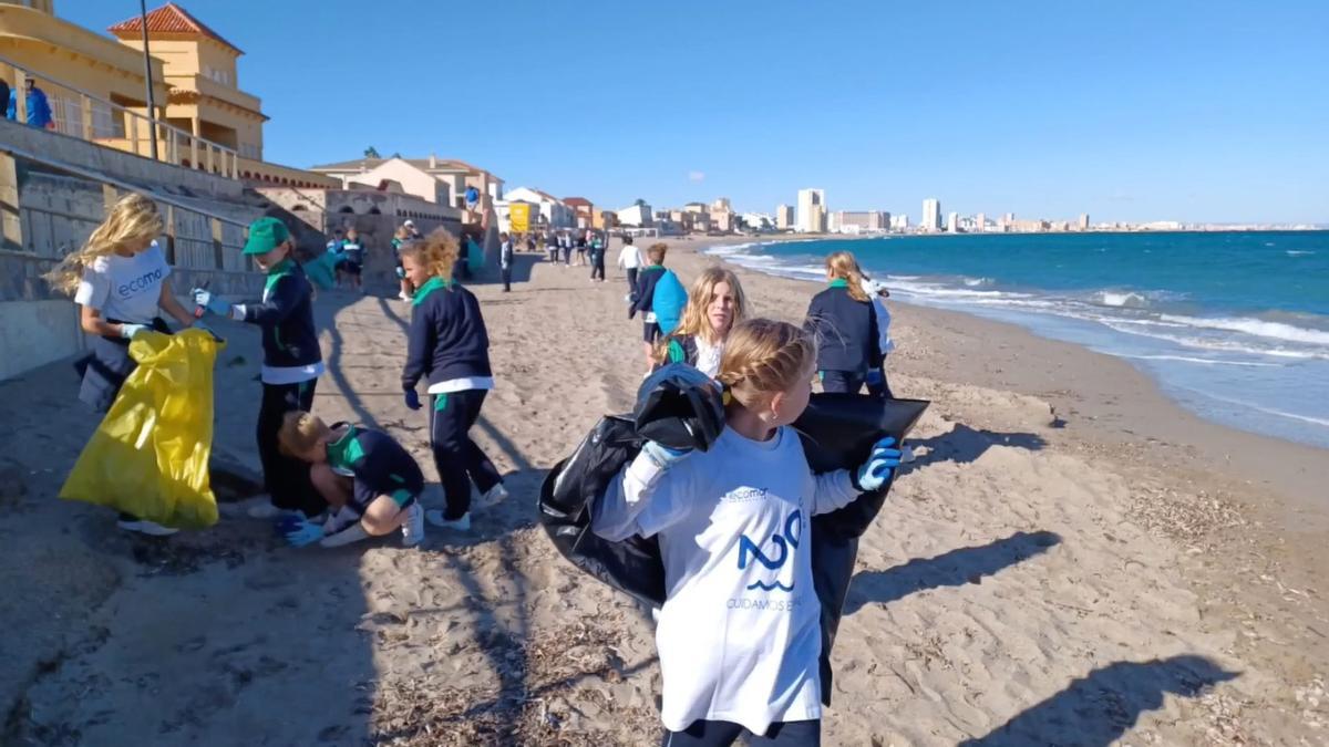 Un grupo de alumnos recoge basura de una playa.