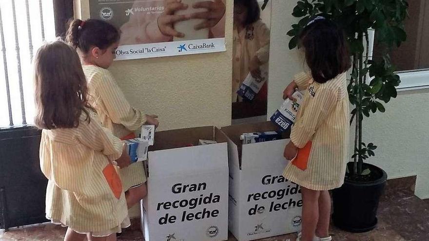 Tres niñas depositan bricks de leche en el punto de recogida en el colegio.