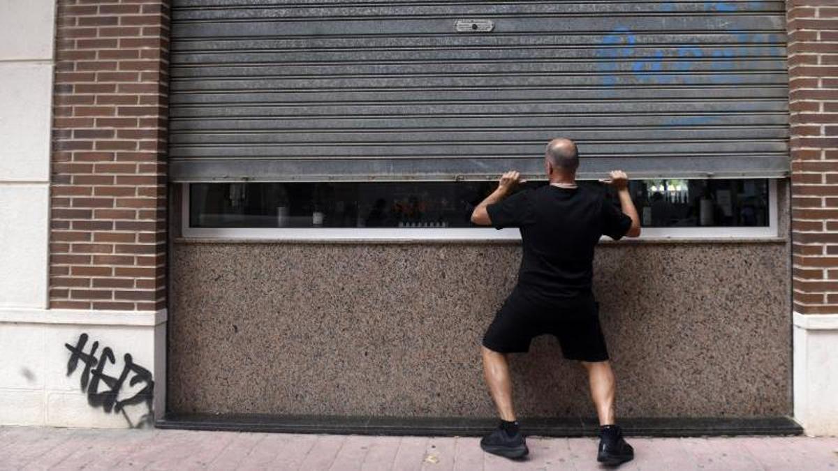 Un autónomo subiendo la persiana de su negocio, en Murcia.