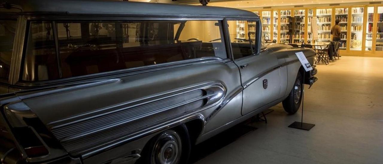 Al fondo, Adrià Terol consulta unos libros en la biblioteca funeraria instalada en el cementerio de Montjuïc, junto a la colección de carrozas fúnebres. En primer plano, un Buick del 58 con su ataúd.