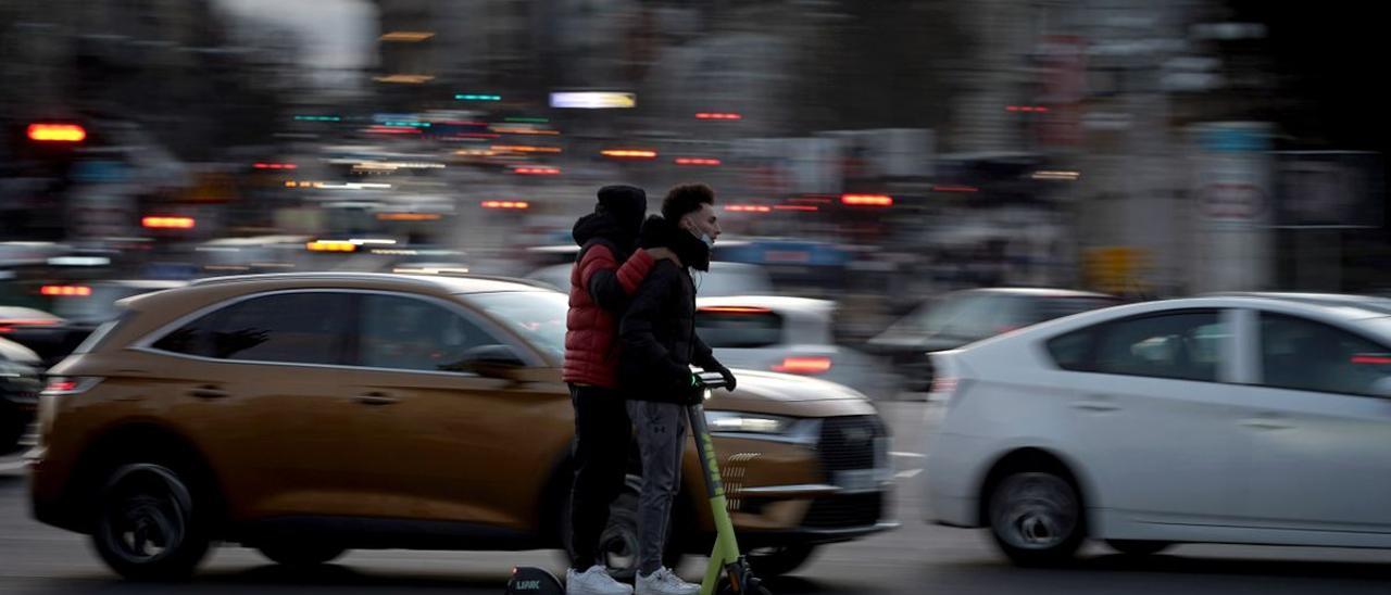 Dos jóvenes desafían al tráfico con un patín eléctrico en el centro de Madrid.