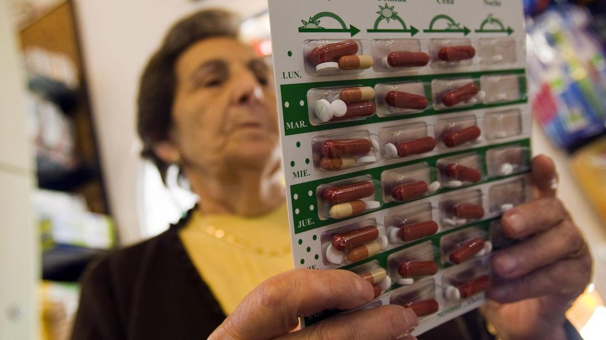 Una mujer mayor observa su pastillero con la medicación de la semana