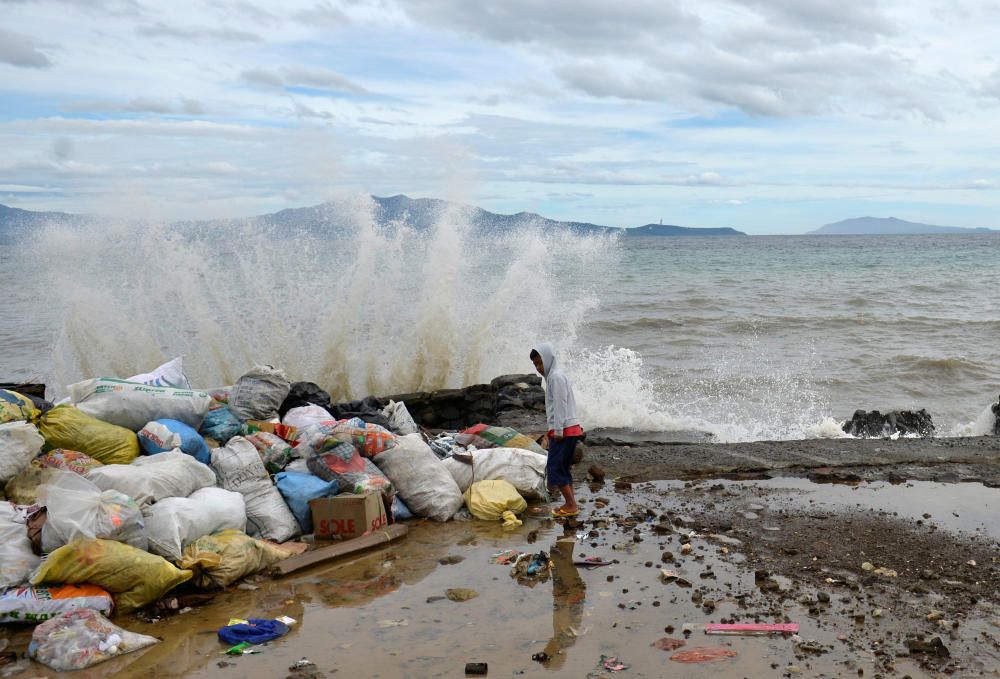 Un joven permanece de pie en un puerto dañado tras el tifon Nock-Ten mientras las olas golpean la orilla.