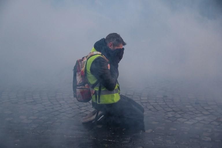 Un manifestante se protege de los gases lacrimógenos durante la manifestación de los 'chalecos amarillos' cerca de los Campos Elíseos, en París. 15 de diciembre de 2018. Zakaria ABDELKAFI / AFP