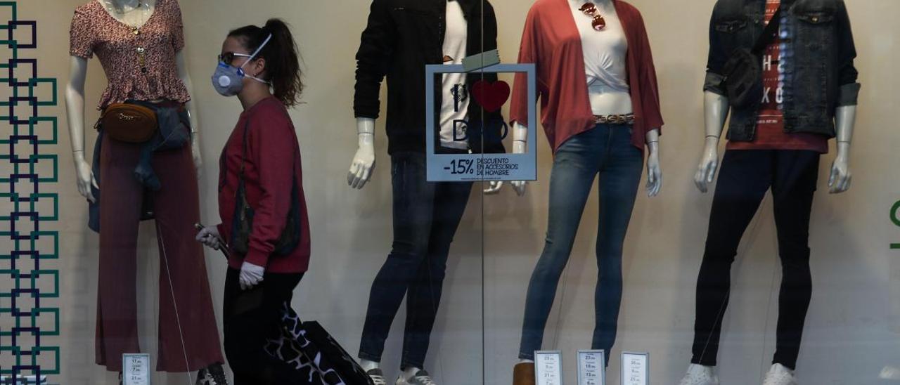 Una joven con mascarilla camina por delante de un escaparate.