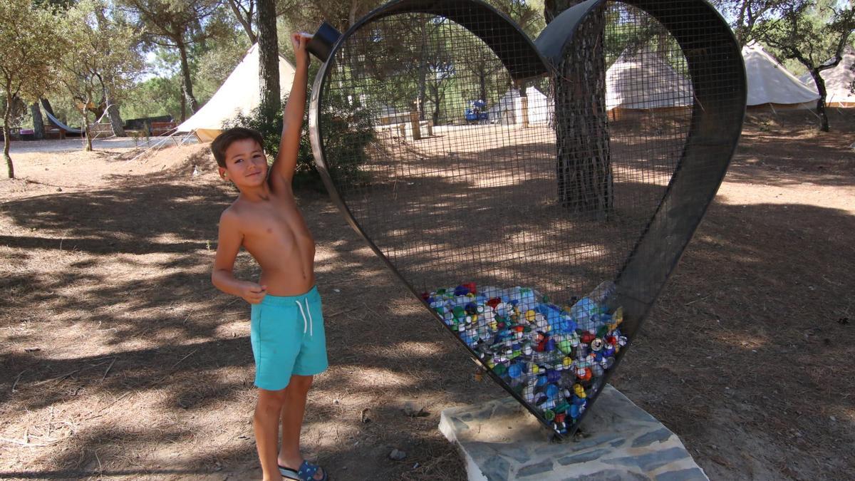 Un niño deposita un tapón en el corazón de reciclaje del cámping Los Villares.